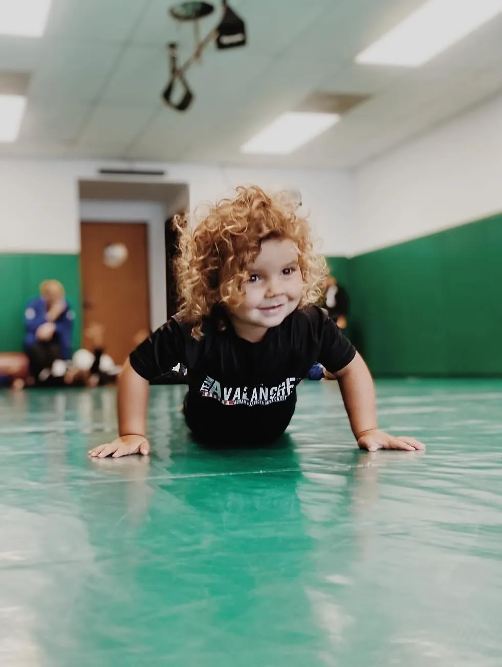 A young student in a Team Avalanche shirt smiling on the mat during a kids' class at Boran Brazilian Jiu-Jitsu