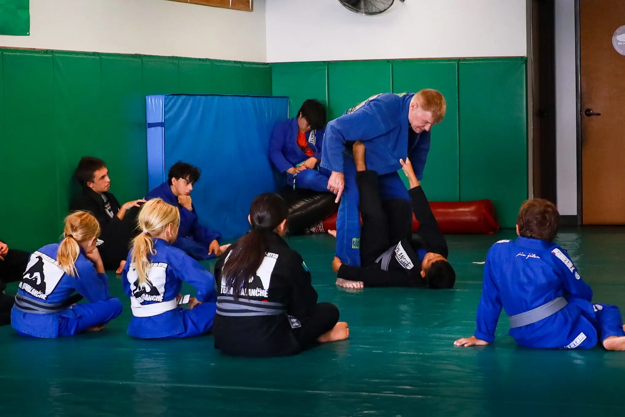 Professor James Boran demonstrating a technique on a student while the class watches from a circle around them