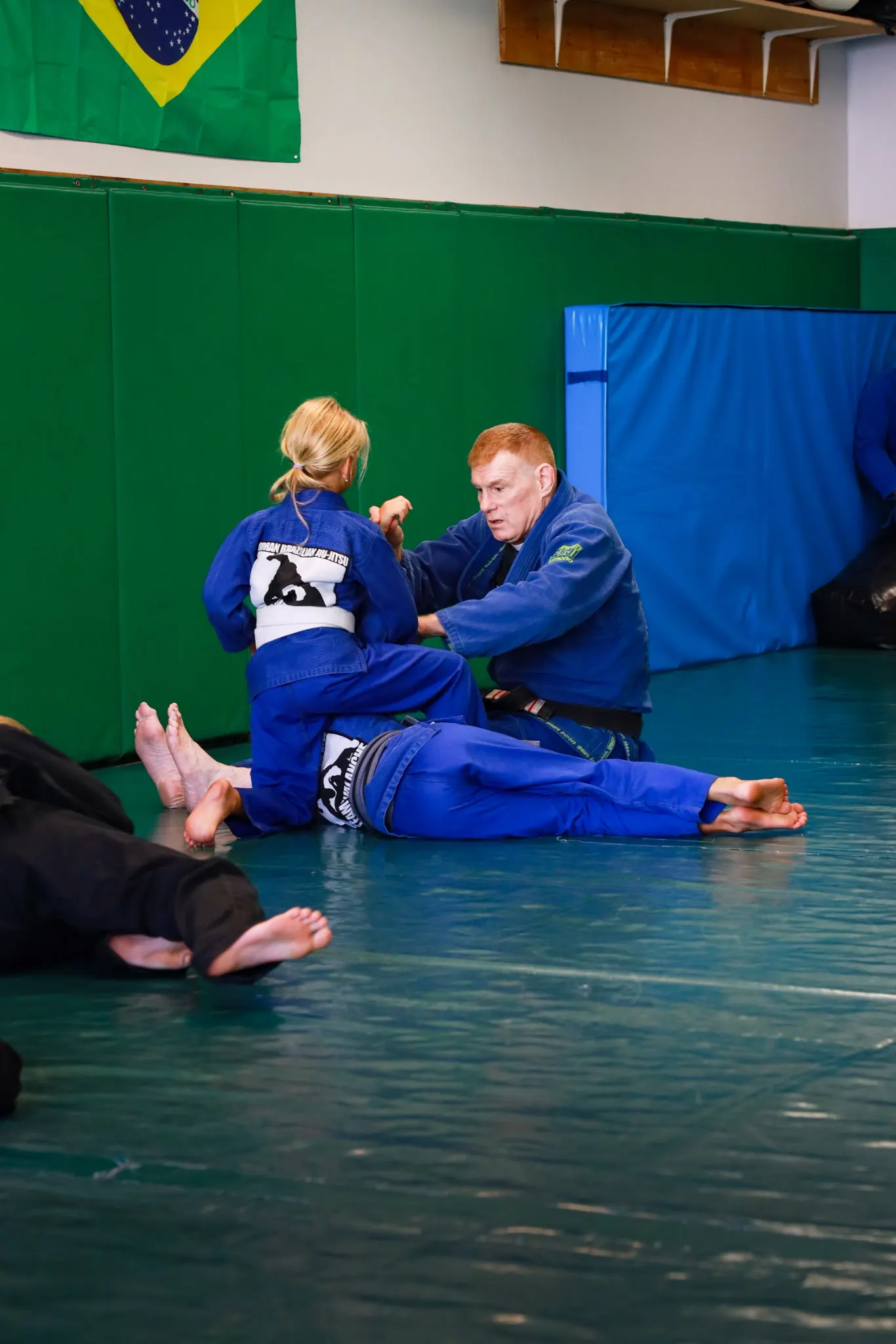 Professor James Boran seated on the mat working one-on-one with a young student during class