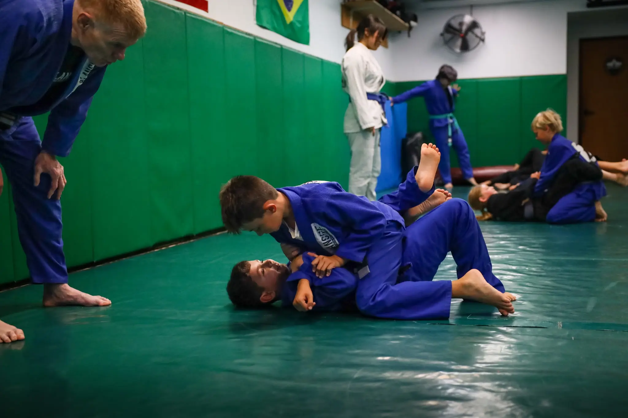 Professor James Boran bending low to watch two young students rolling, one holding top position, with the class rolling behind them